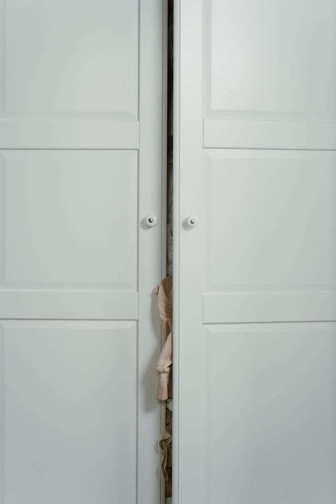 White wardrobe with slightly open doors revealing clothing inside, emphasizing simplicity and elegance.