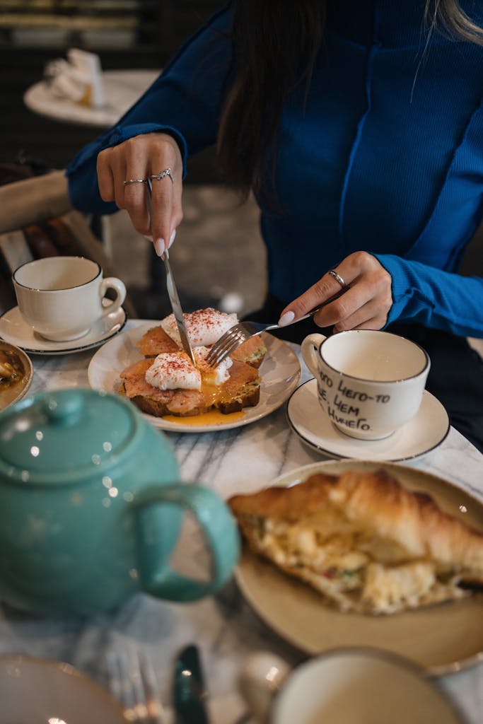 Woman enjoying breakfast with poached eggs, toast, and tea in a cozy setting.