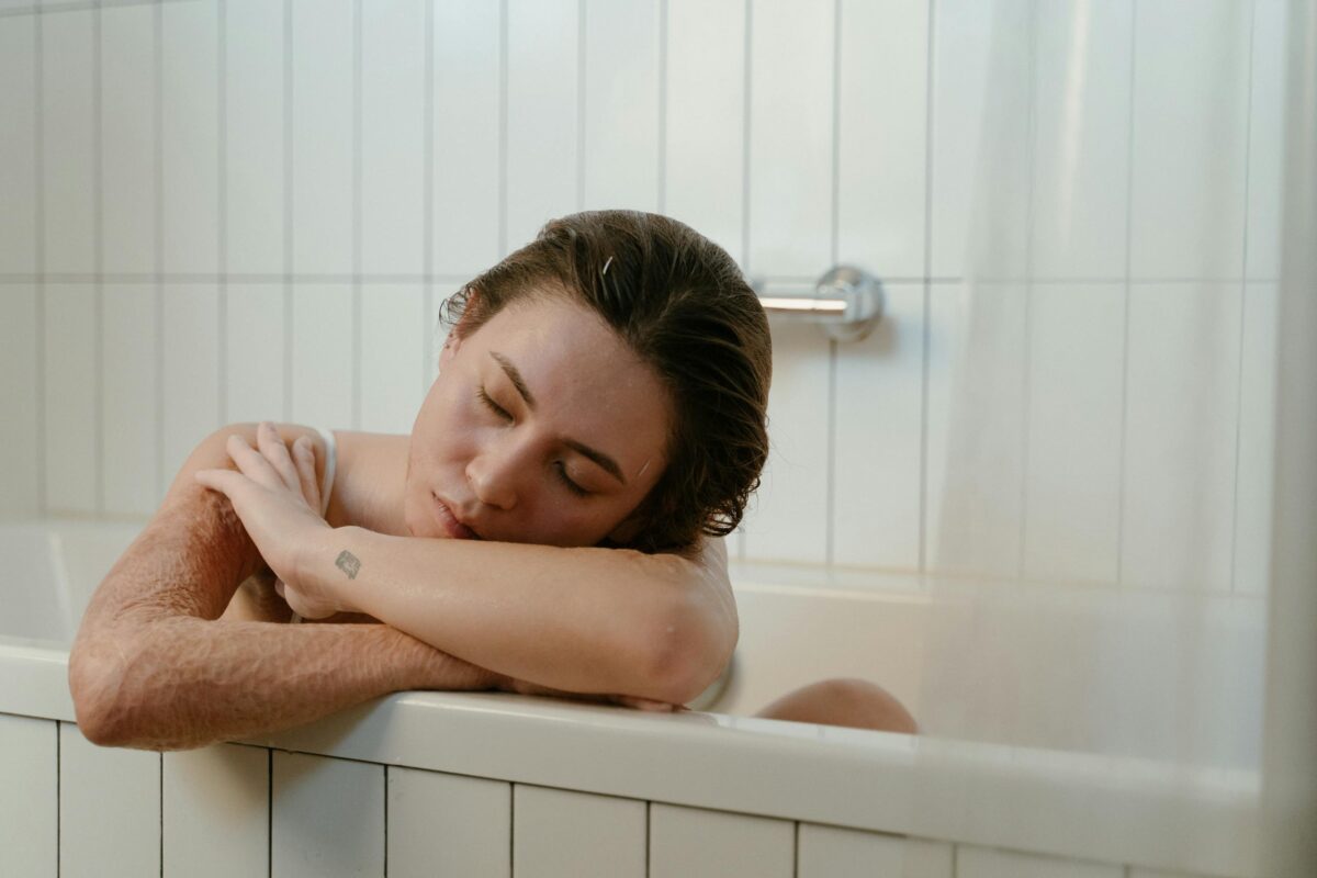 Woman with closed eyes resting in a bathtub, embodying self love and relaxation.