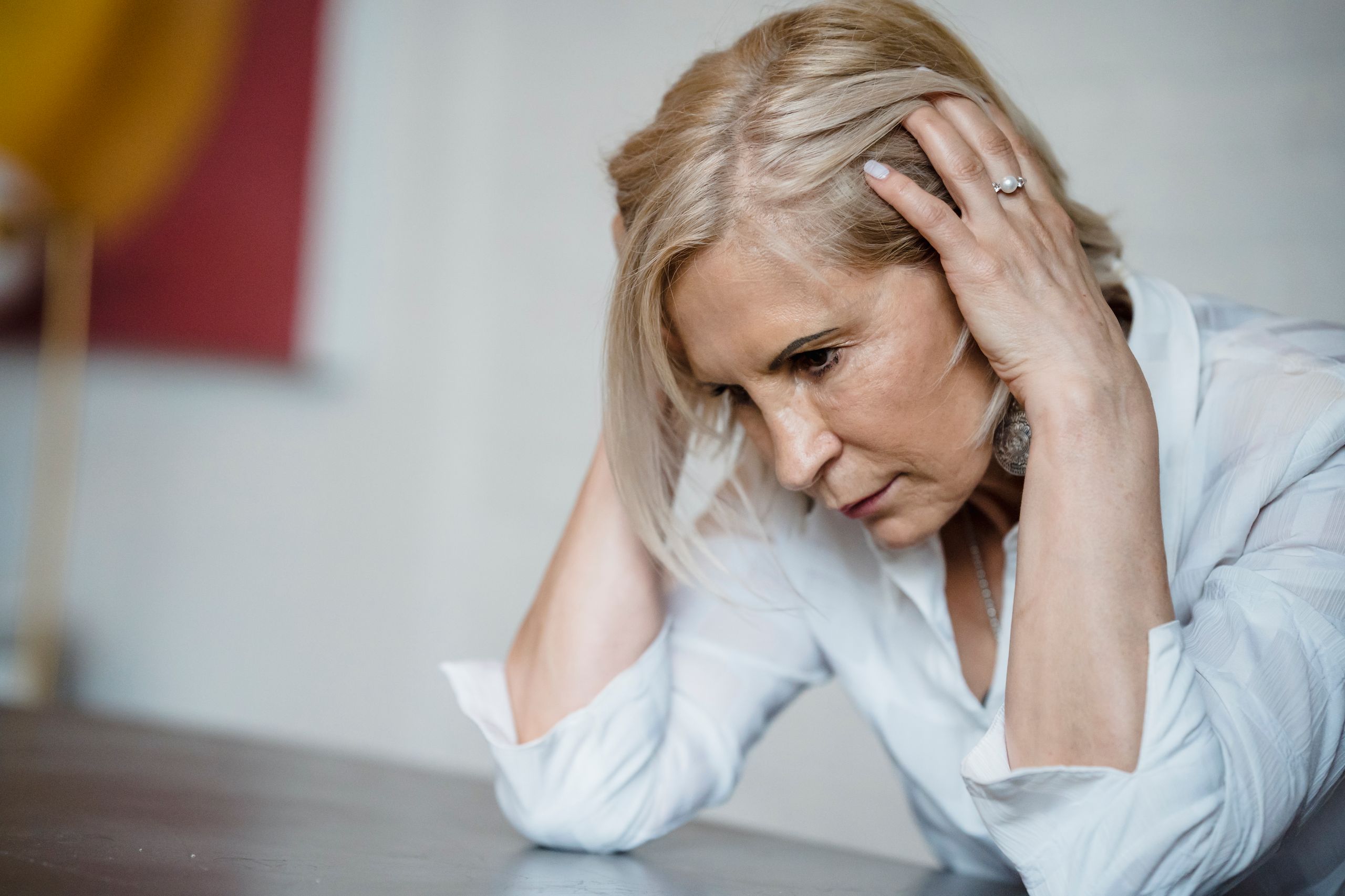 Woman with long blonde hair, deep in thought, wearing a white blouse indoors.