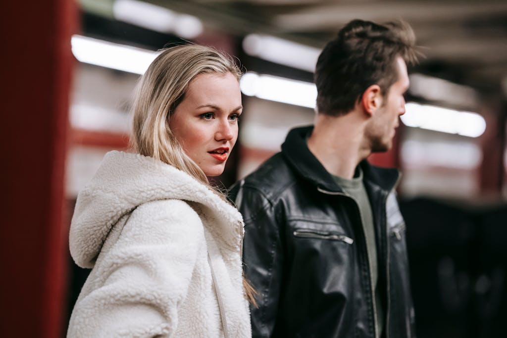 Young couple in warm casual clothes standing together in metro and looking away