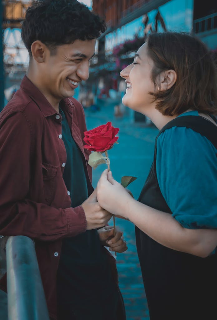 Young couple laughing and sharing a rose on a city street, capturing a romantic moment.