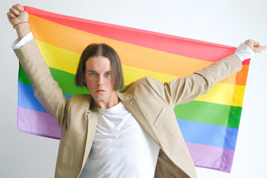 Young man in beige suit proudly holding a rainbow flag symbolizing LGBT pride and identity.