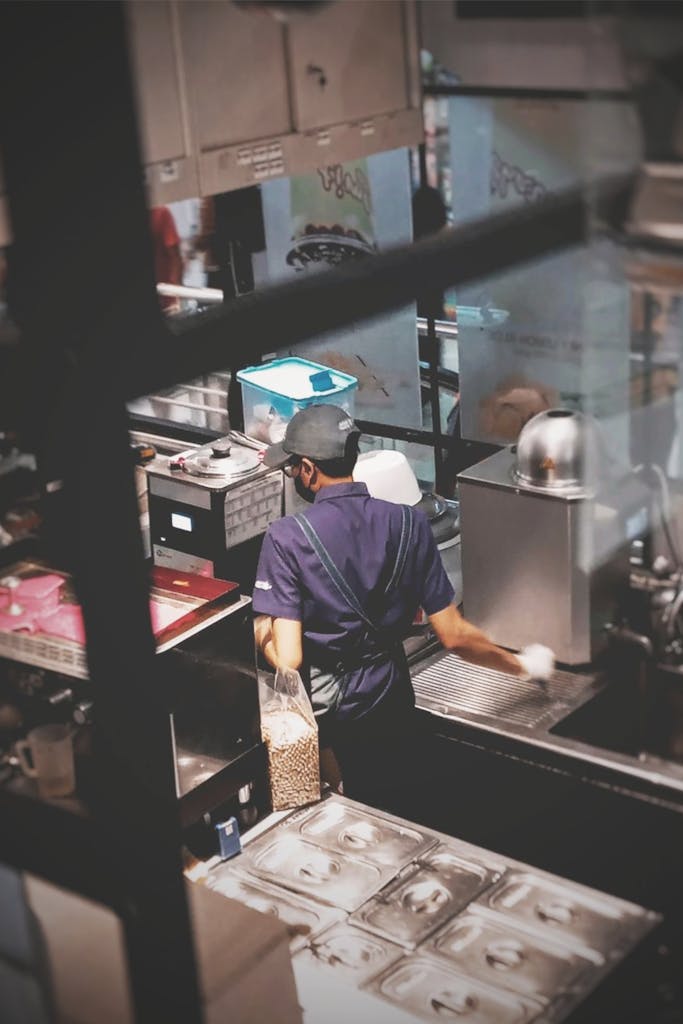 Young worker in an industrial kitchen preparing food, wearing a uniform.
