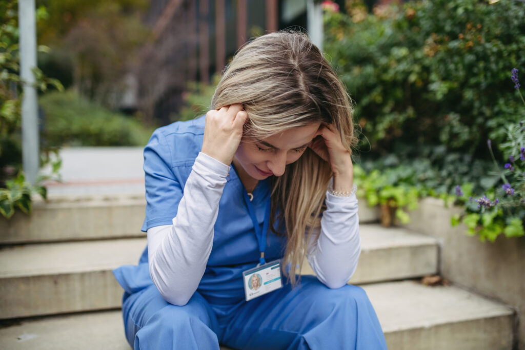 Female doctor feeling overwhelmed at work, sitting on stairs. Healthcare workers having stressful job, feeling exhausted. Burnout syndrome for doctors and nurses.