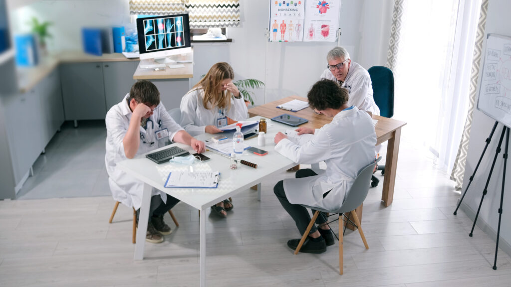 A group of researchers in white coats are sitting at a table in an office of the hospital. A meeting at the clinic. Doctors are developing a new drug