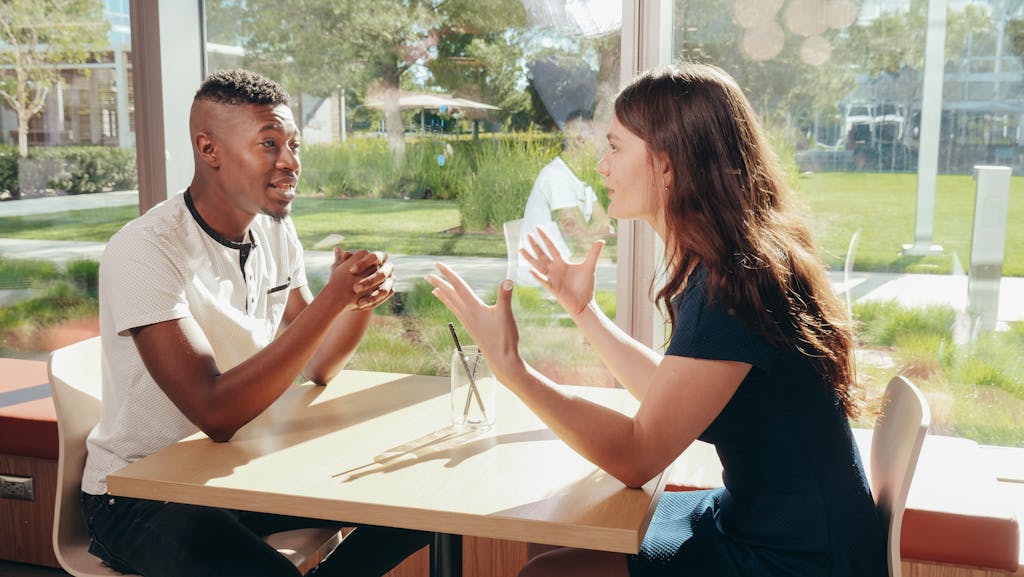 A black man and caucasian woman having an engaging conversation at a cafe table indoors.