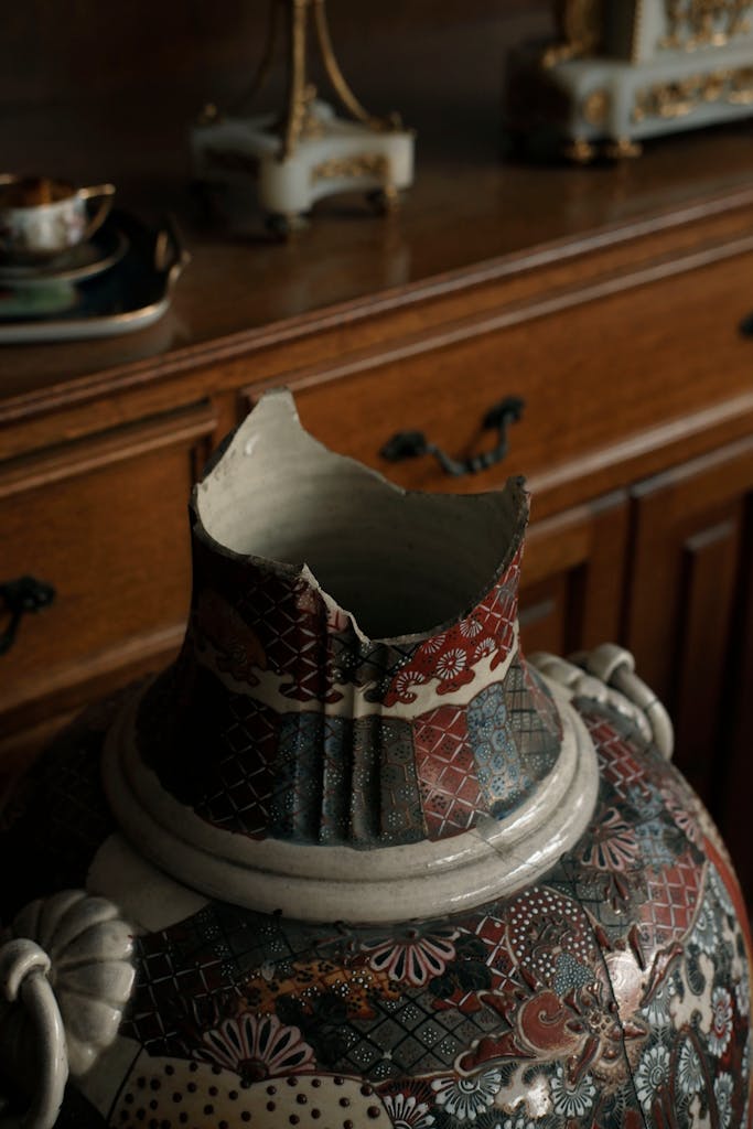 A broken antique vase with oriental pattern in a dimly lit museum setting for artistic appeal.