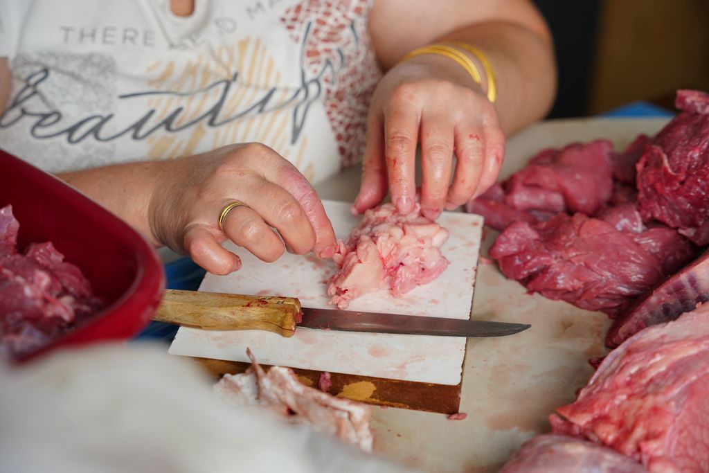 A butcher meticulously trimming fresh cuts of meat on a counter indoors with a knife.