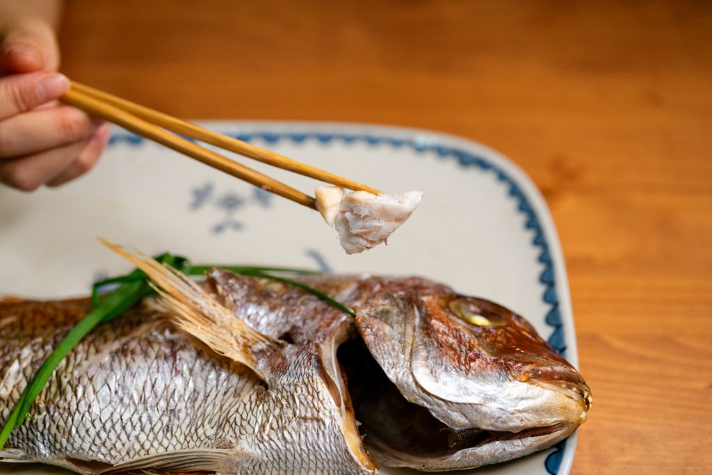 A close-up of a traditional Asian grilled fish served on a decorative plate with chopsticks.