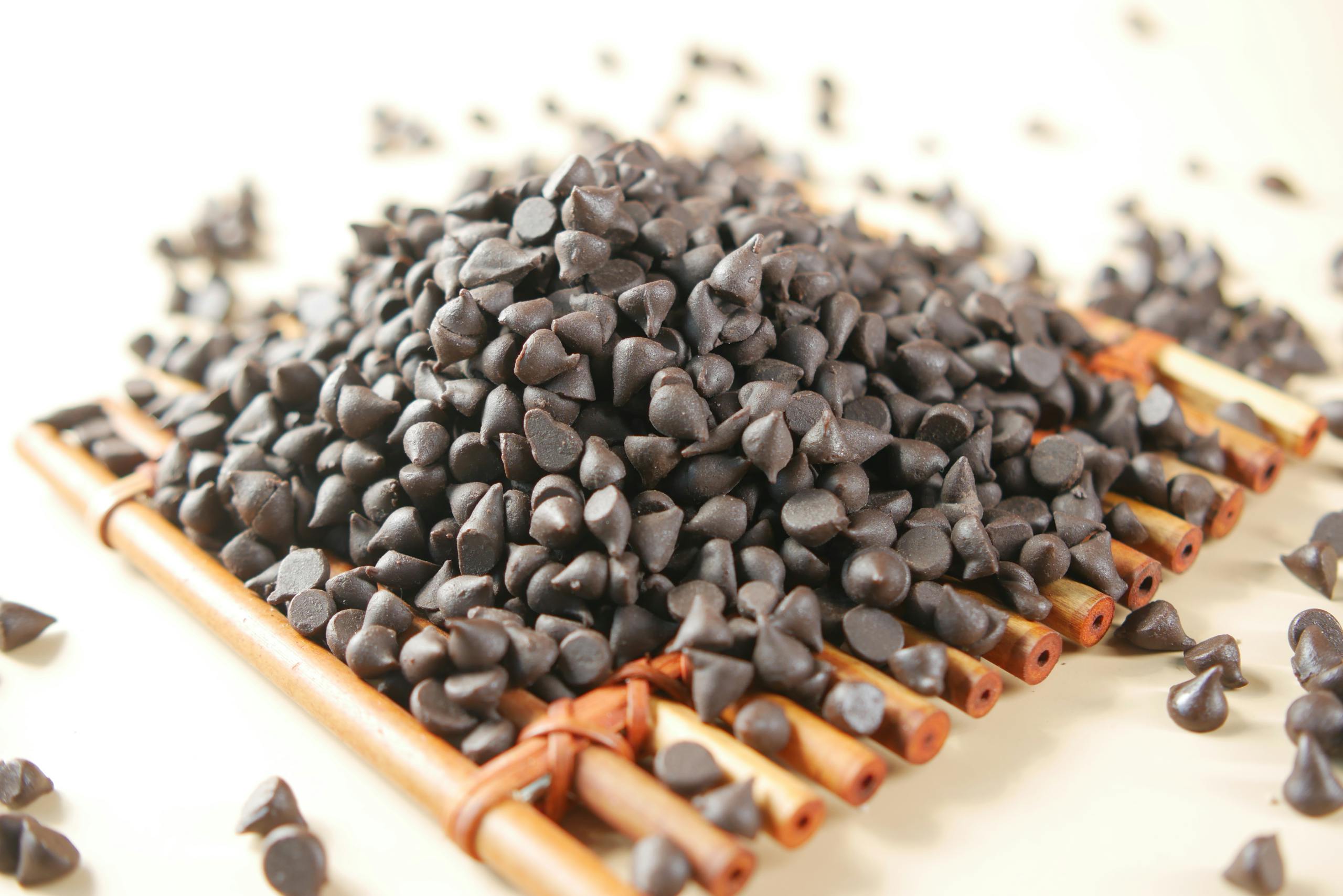 A detailed shot of rich, dark chocolate chips scattered on a rustic wooden tray, perfect for food photography.