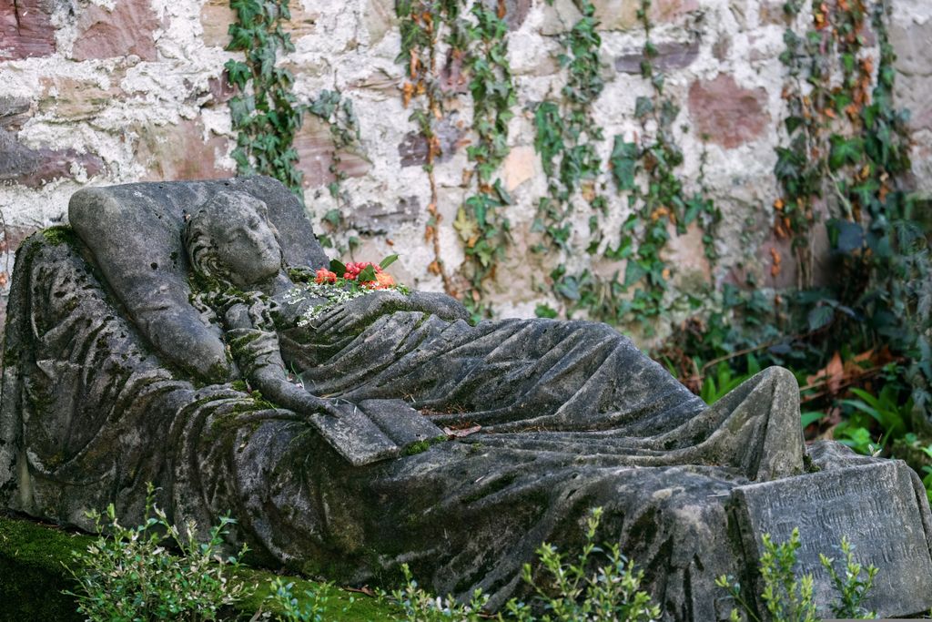 A detailed stone sculpture of a reclining figure in Freiburg's historic cemetery, surrounded by ivy.