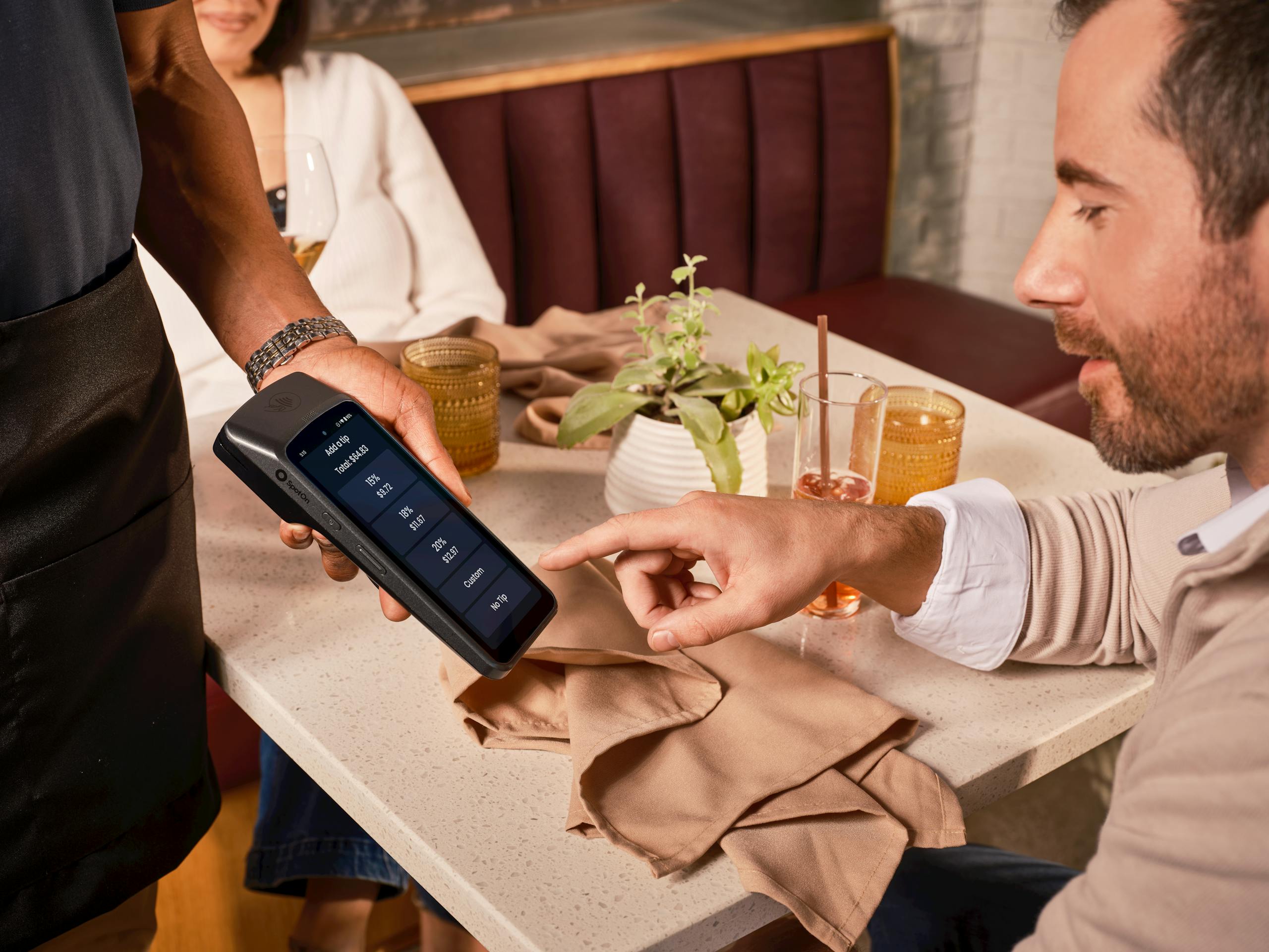 A diner uses a handheld POS system for digital tipping in a casual restaurant setting.