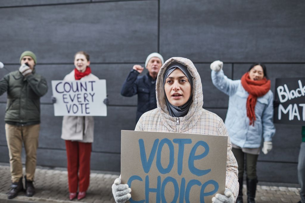 A diverse group of activists protest for voting rights with signs outdoors. Includes signs like 'Vote Choice' and 'Count Every Vote.'
