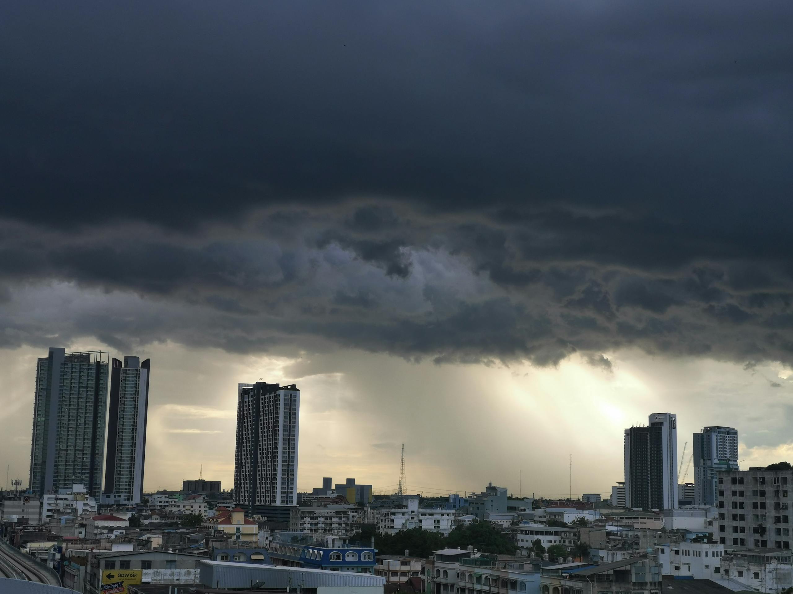 A dramatic cityscape view with tall buildings under a stormy sky with rain and sunlight peeking through.