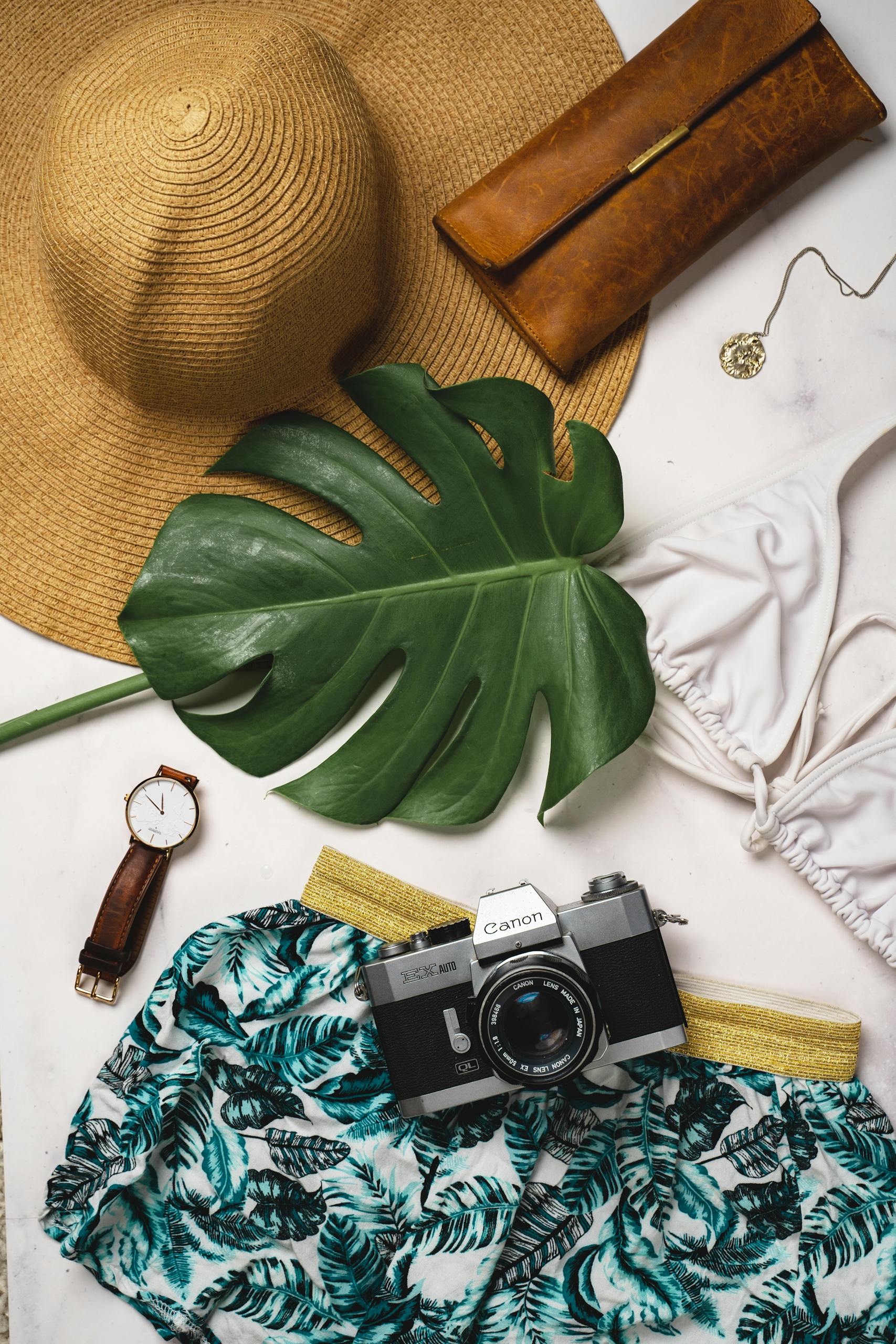 A flat lay of beach essentials including a straw hat, swimsuit, and vintage camera.