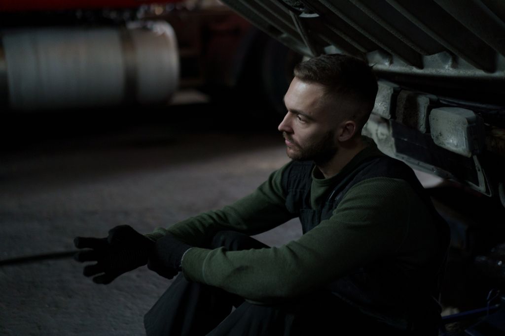 A focused auto mechanic in deep thought during a work break in a dimly lit workshop.