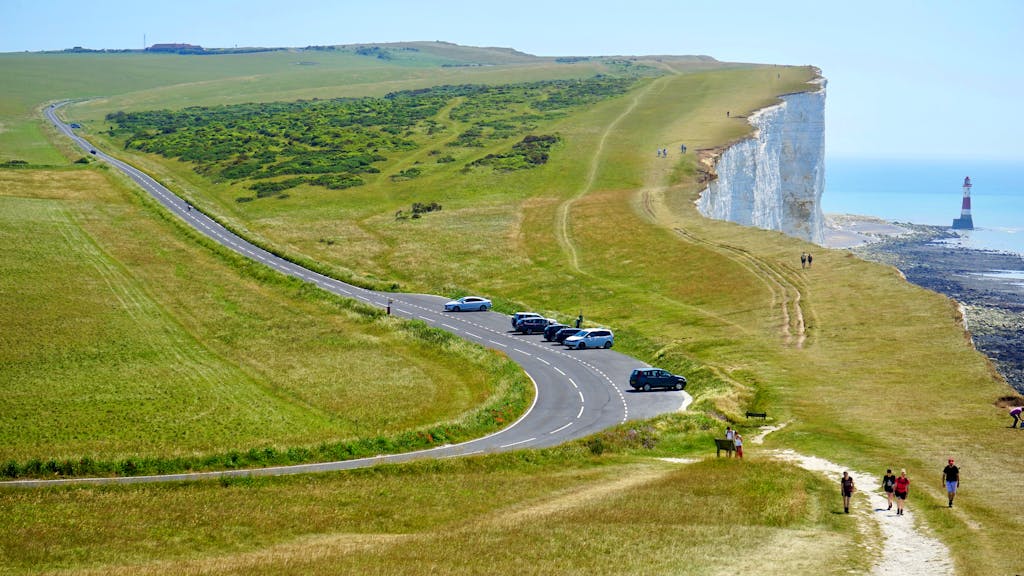 A picturesque coastal road with a lighthouse on cliffs under a clear summer sky.