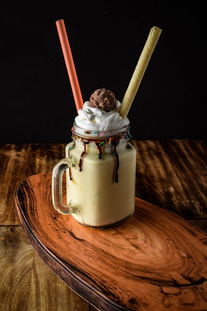 A rich milkshake topped with whipped cream, chocolate drizzle, and wafer sticks in a mason jar.