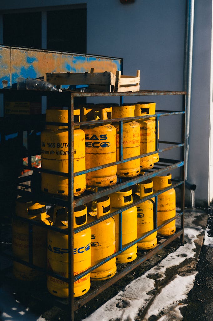 A row of yellow gas cylinders in a metal rack outside, against a wall.