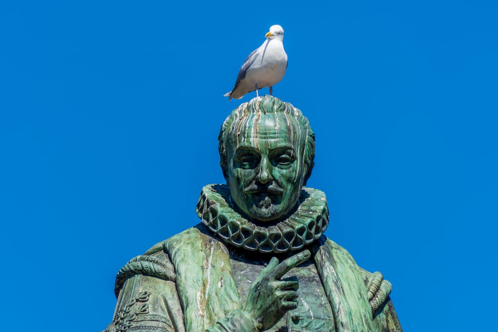 A seagull perched atop a historical bronze statue under a clear blue sky, capturing a humorous and artistic moment.
