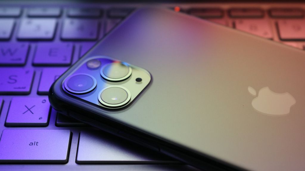 A smartphone with a triple camera setup placed on a colorful lit keyboard in a close-up view.