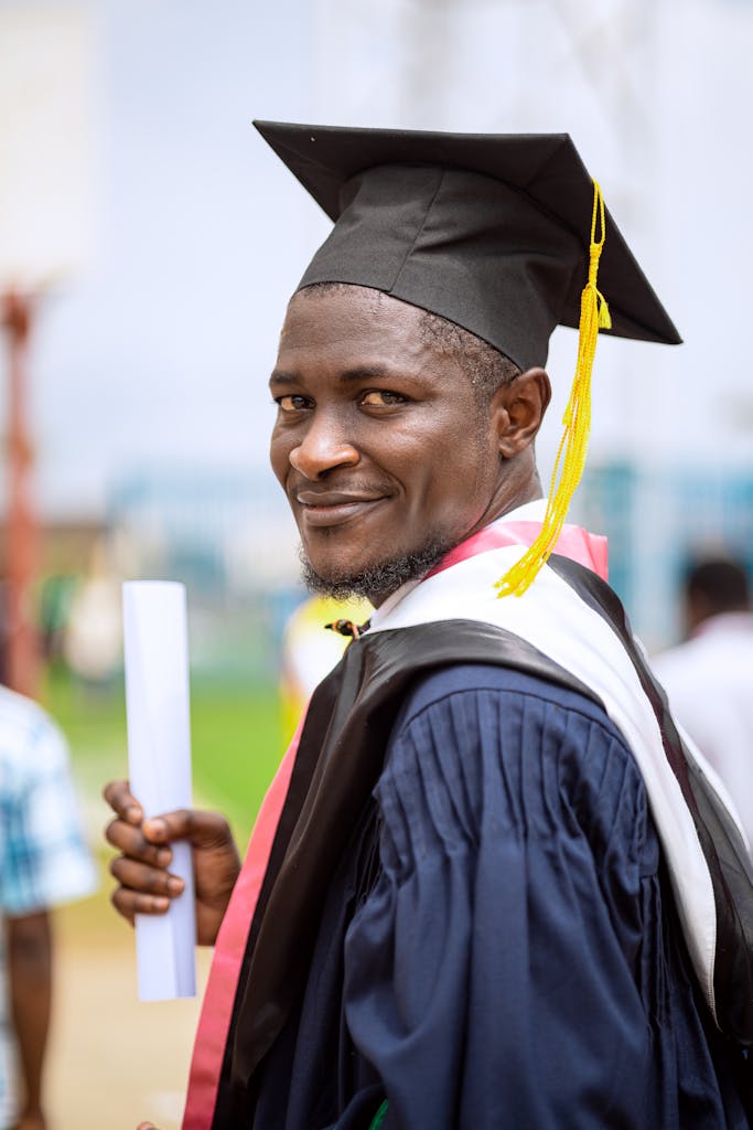 A smiling male graduate with a diploma celebrates his achievement outdoors.