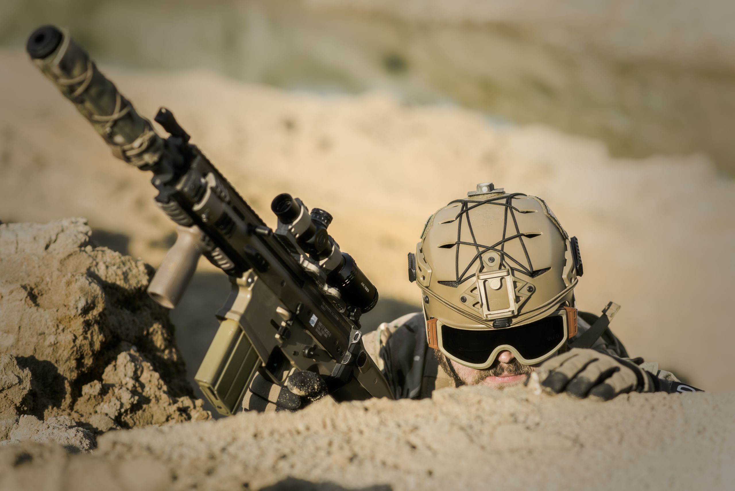 A soldier with tactical gear hiding in the desert, poised for action.