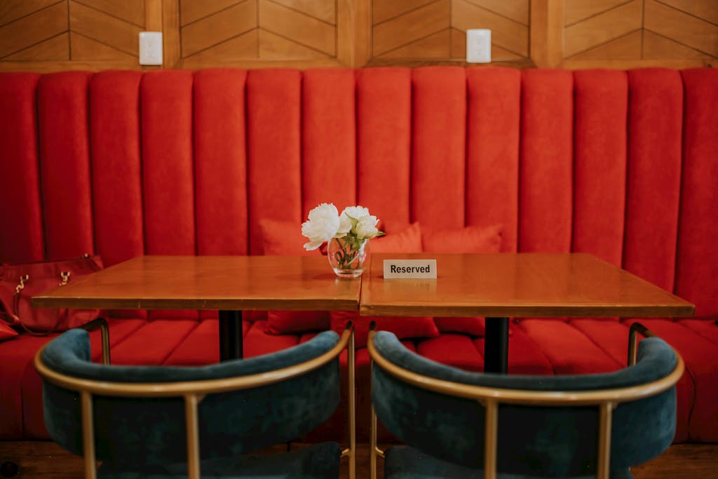 A stylish café setup featuring red upholstered seating, a reserved table, and a vase of white flowers.