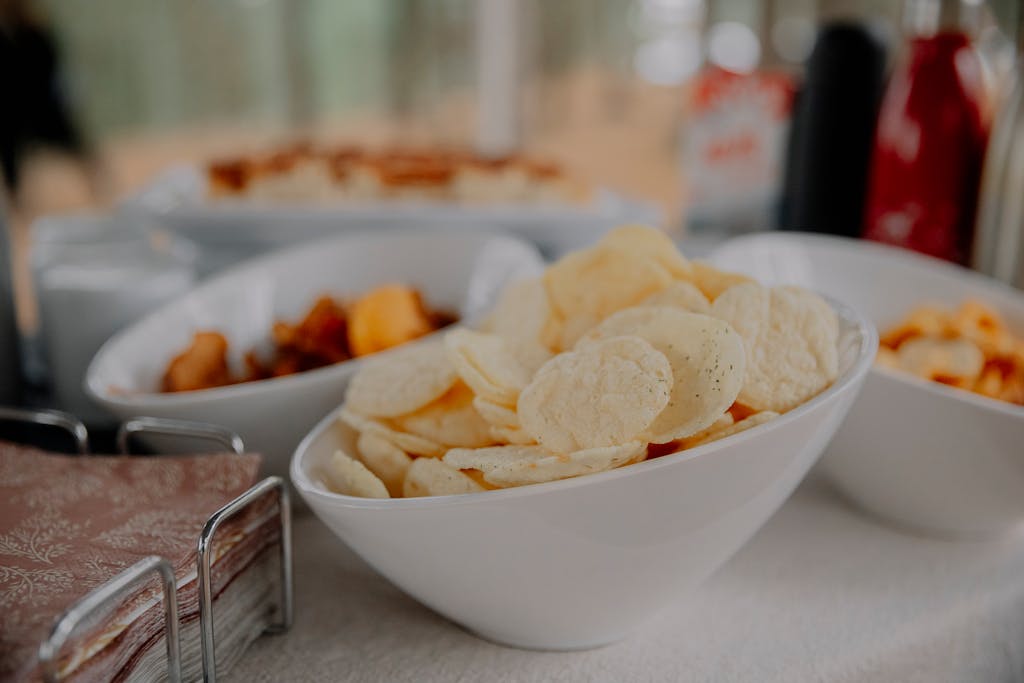 A variety of chips served in white bowls on a table, perfect for party snacks.