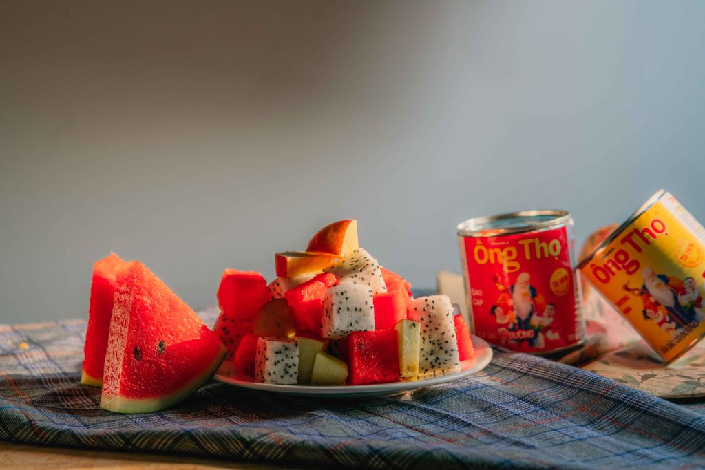 A vibrant display of cut watermelon and dragon fruit with condensed milk cans on a cloth.