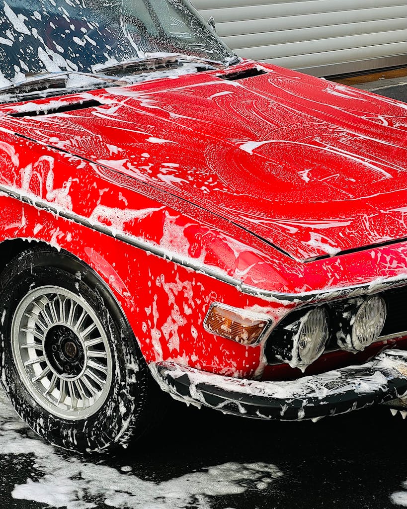 A vibrant red classic car being washed with foam, highlighting its vintage appeal.