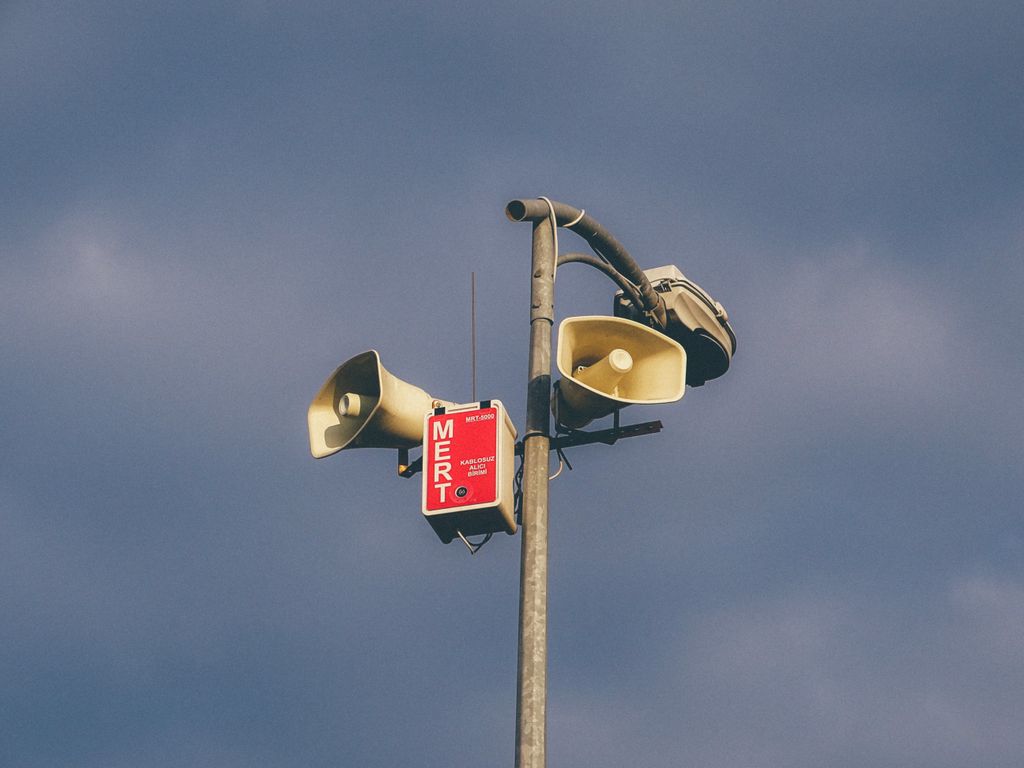 A warning system with loudspeakers on a pole against a cloudy sky, signaling emergency alerts.