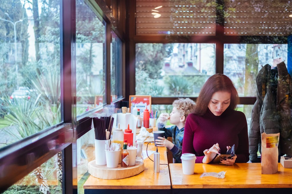 A woman and her son sitting in a cafe, enjoying drinks by a window with a garden view.