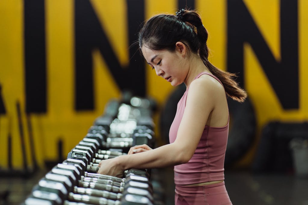 A woman in a gym selecting a dumbbell from a row, representing fitness and choice.