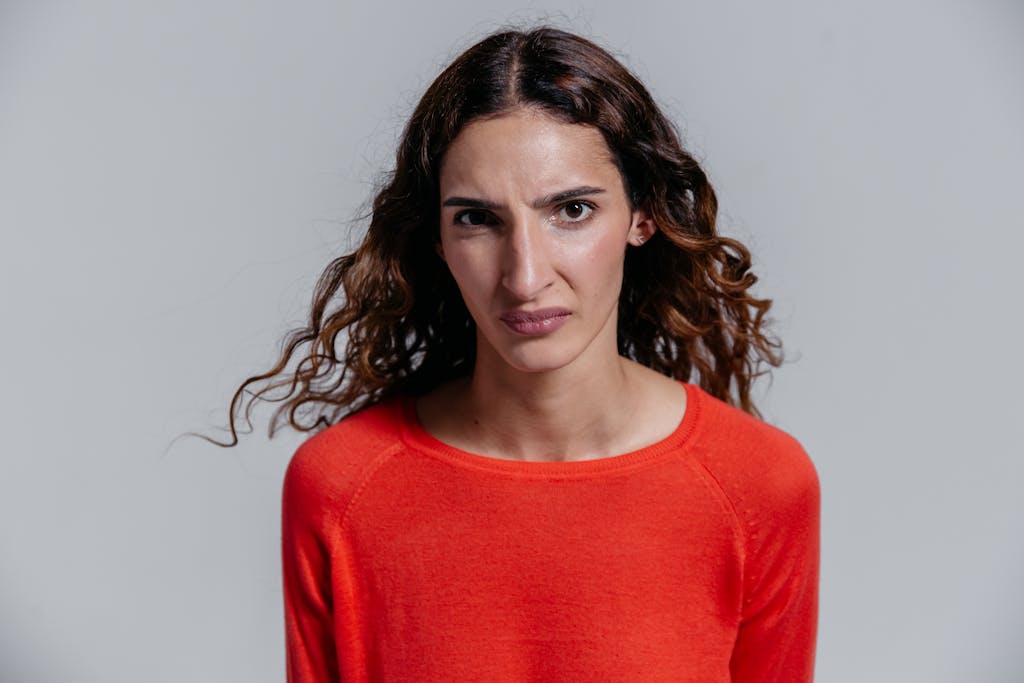 A woman in a red sweater showing a serious and disgusted facial expression.