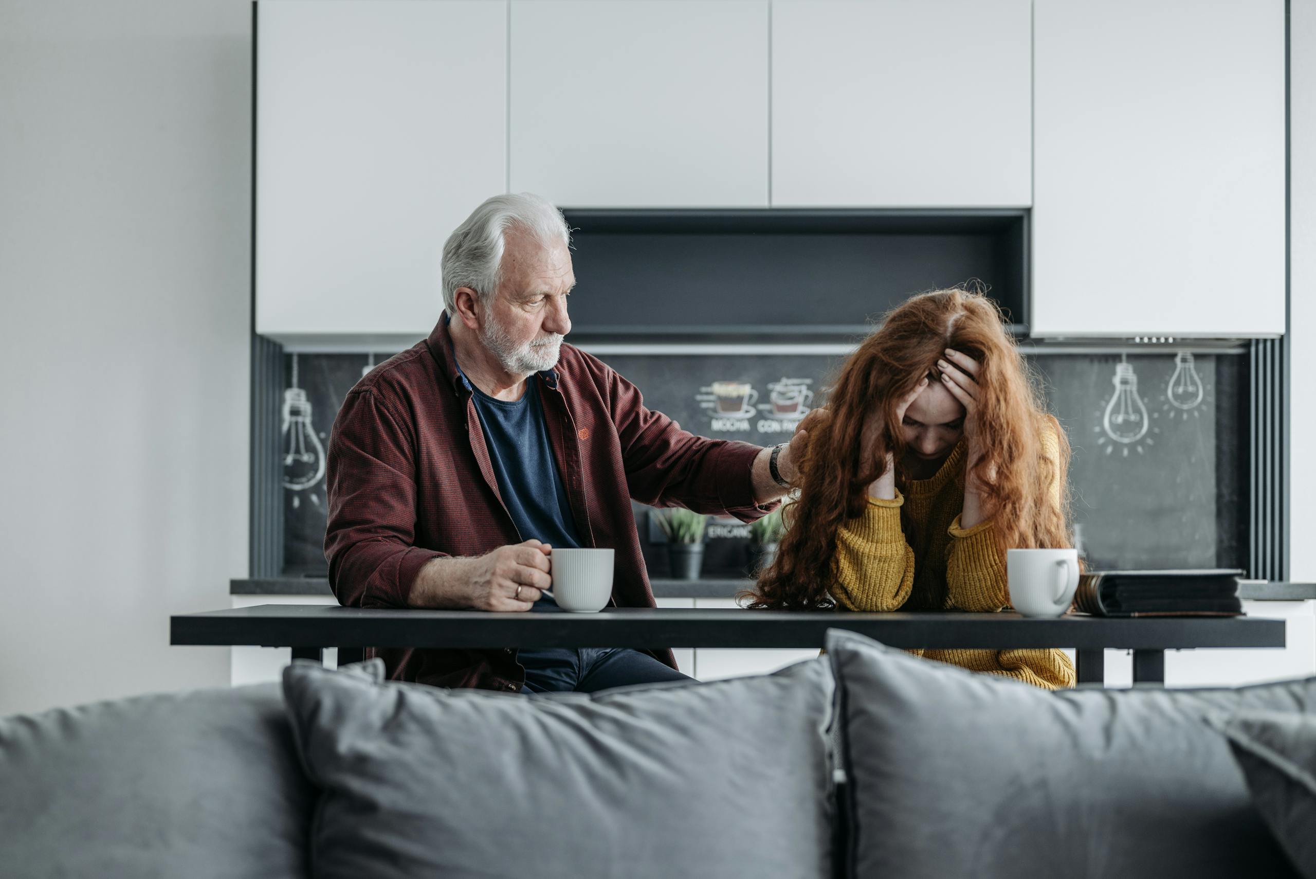 An elderly man comforts a distressed young woman at a kitchen table. Emotional moment captured indoors.