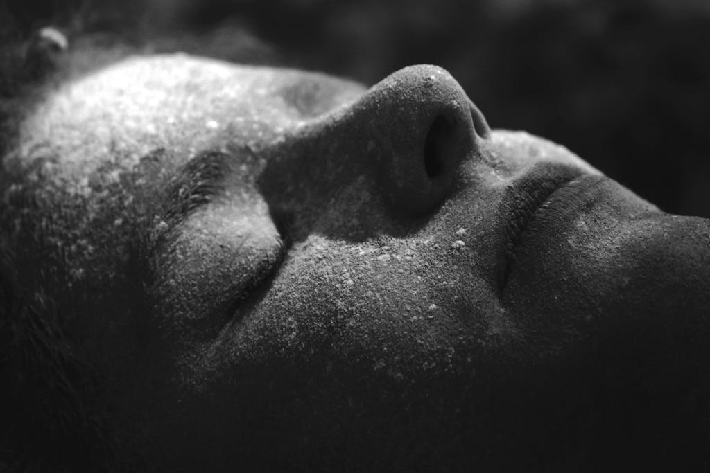 Artistic black and white shot of a serene face with closed eyes and textured skin.