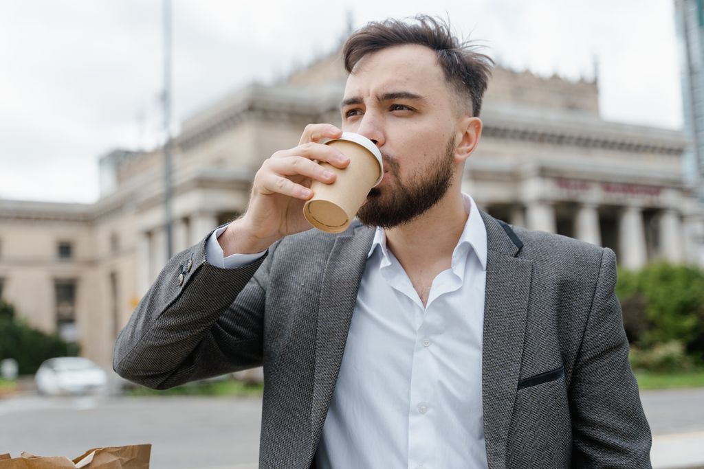 Businessman in a gray suit drinking coffee outdoors near a city building. Vibrant and casual setting.