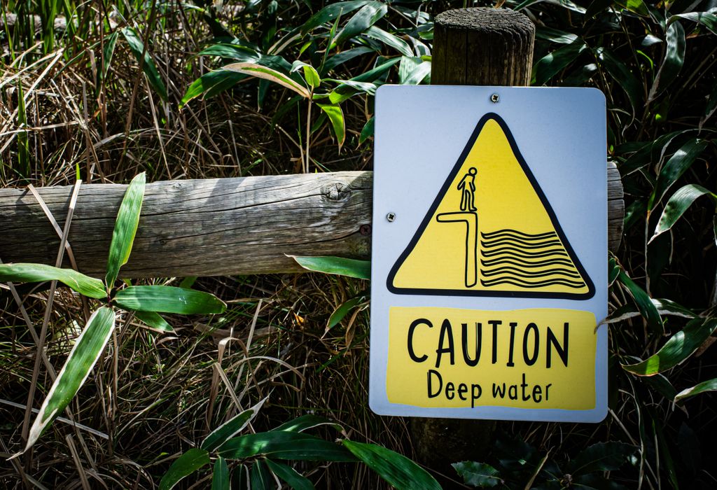 Caution deep water warning sign with a natural background, emphasizing safety near water bodies.
