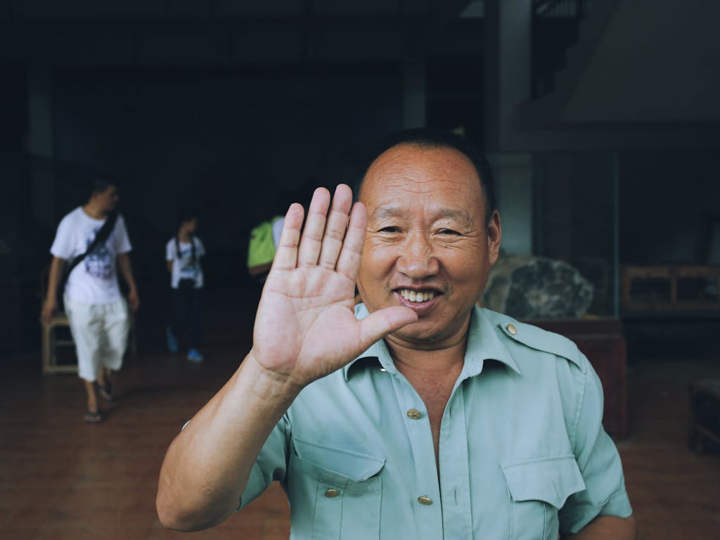 Cheerful man with hand up, smiling in a casual indoor setting.