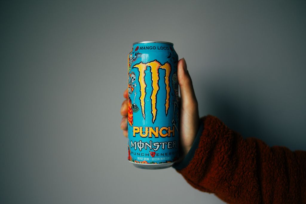 Close-up of a hand holding blue energy drink can against a neutral background.