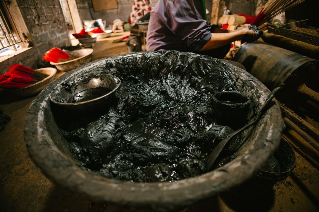 Close-up of a large pot filled with black dye used in traditional incense stick production indoors.