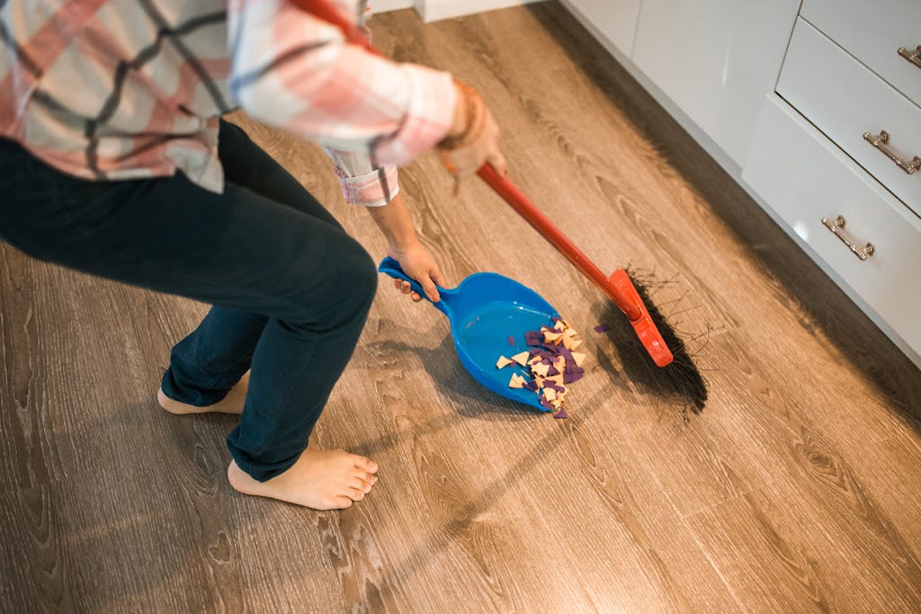 Close-up of a person sweeping debris into a blue dustpan on a wooden floor.