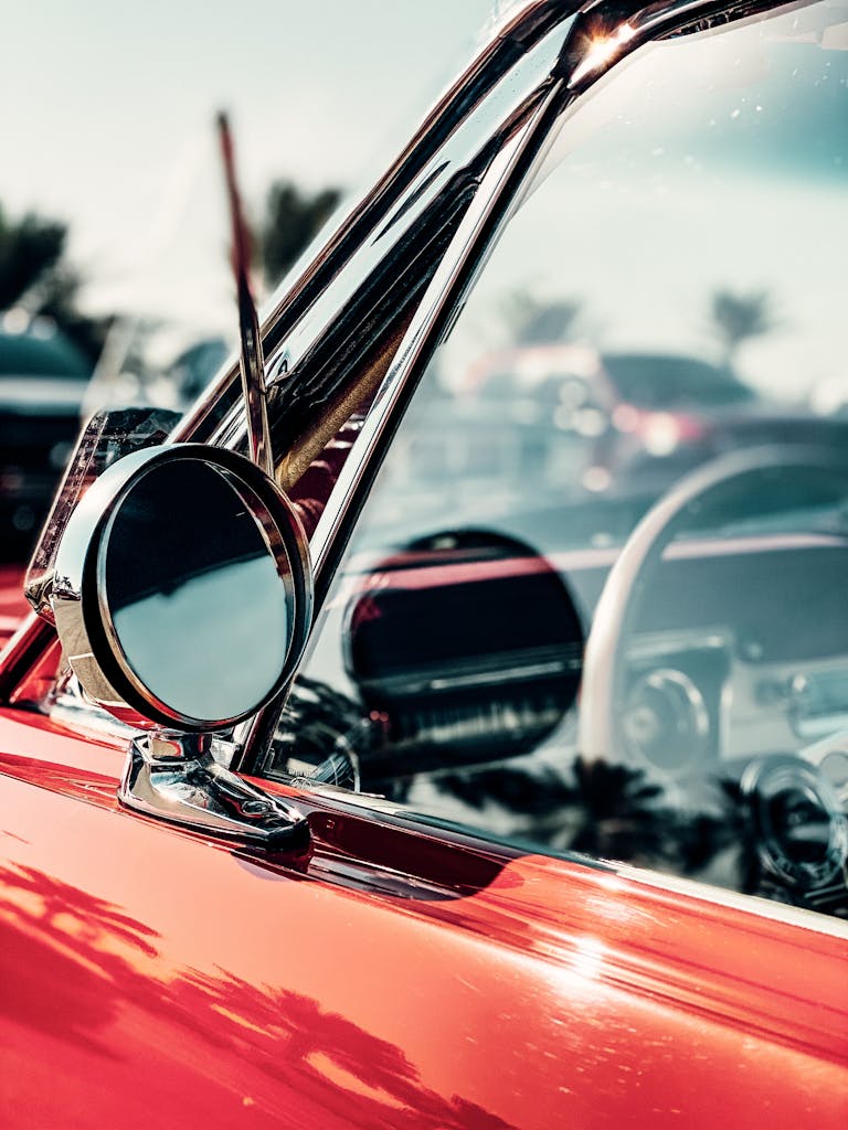 Close-up of a vintage red car highlighting the mirror and window in a classic setting.
