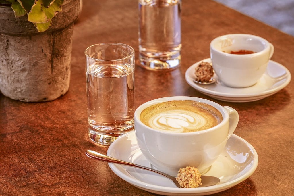 Close-up of latte and espresso with water on rustic table setting, indoors.
