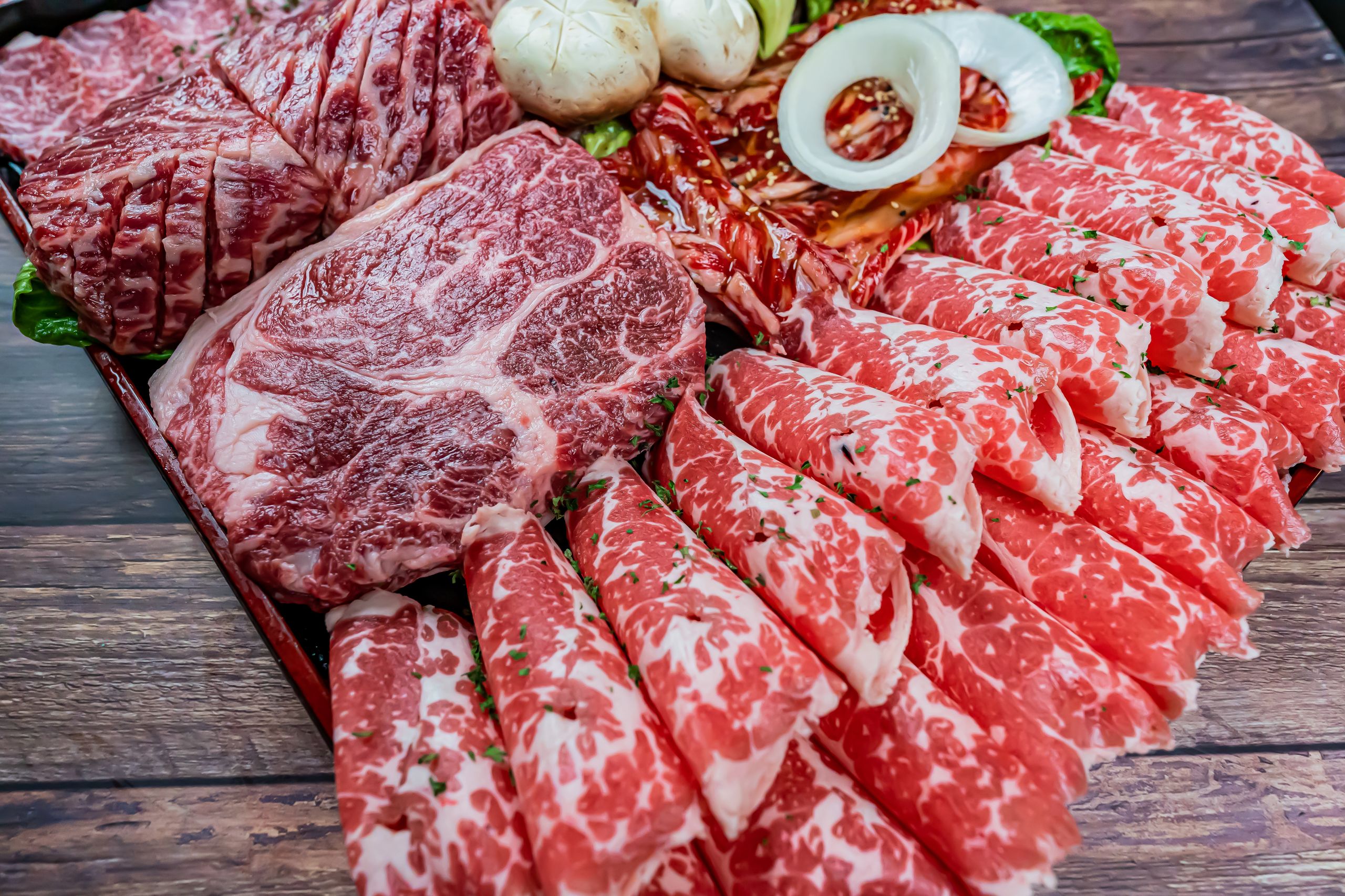 Close-up of marbled raw wagyu beef slices on a wooden tray, ideal for cooking.
