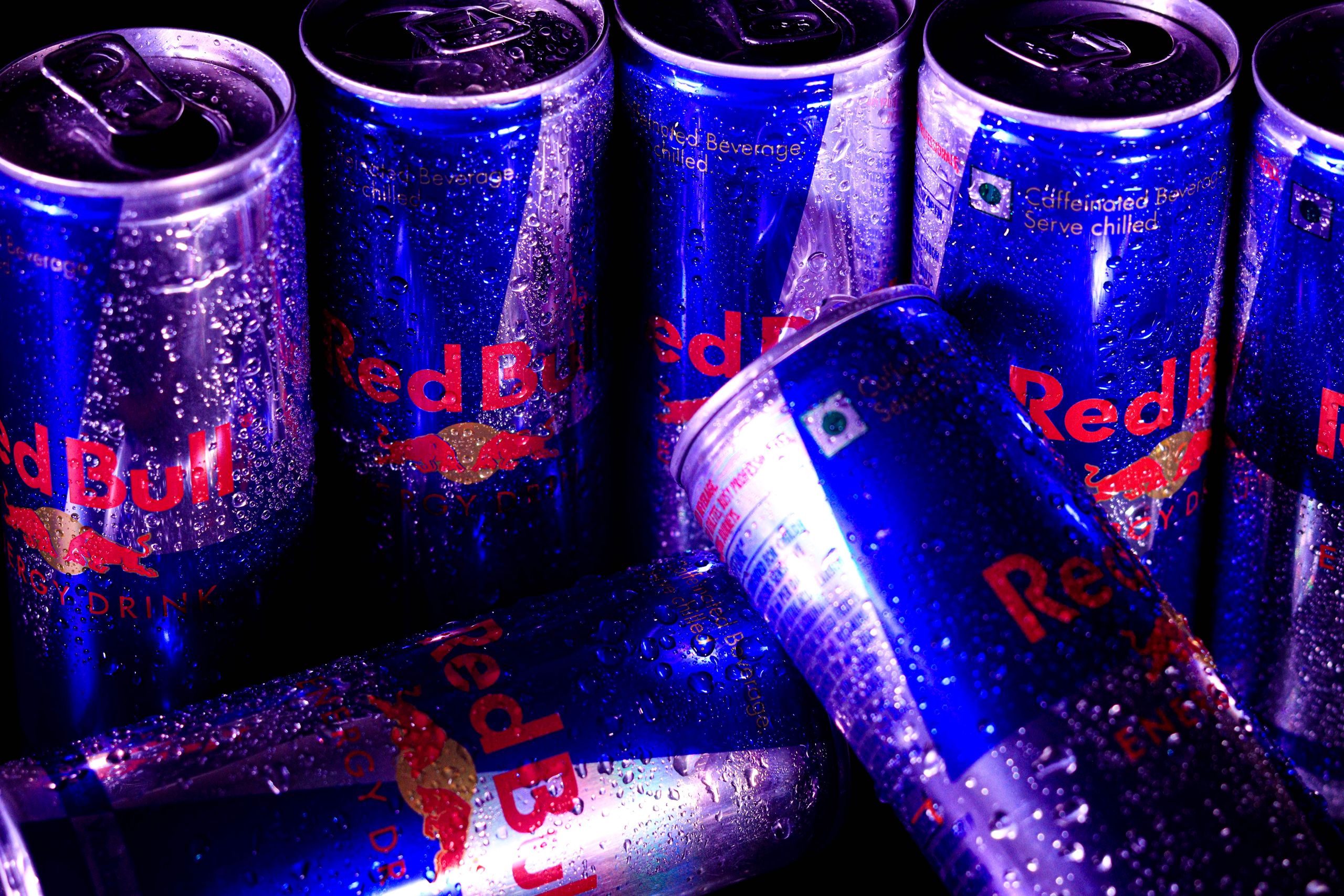 Close-up of multiple Red Bull cans with water droplets, highlighting freshness and energy.