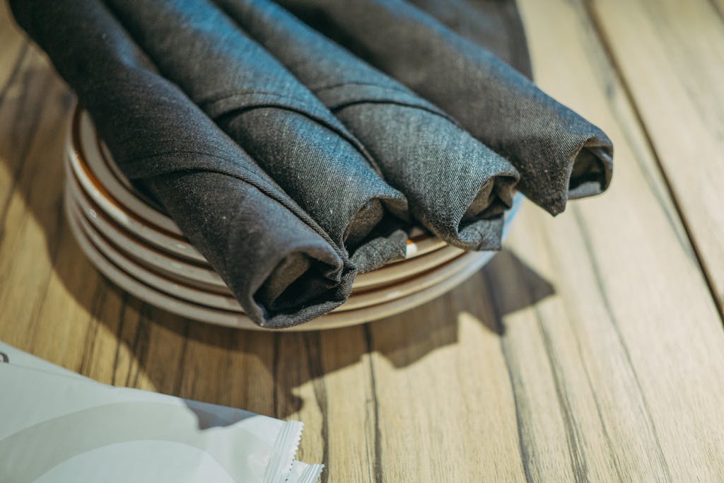 Close-up of stylish rolled napkins arranged elegantly on stacked plates on a wooden table, perfect for dining settings.