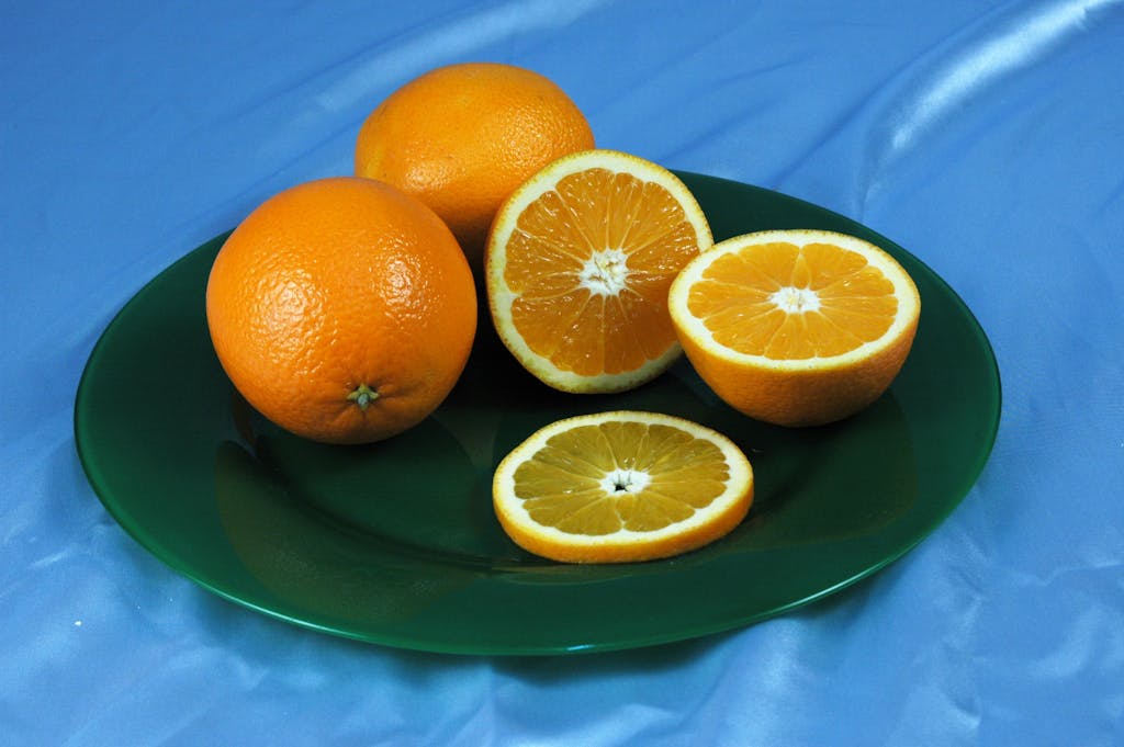 Close-up of whole and sliced oranges on a green plate against a blue background.